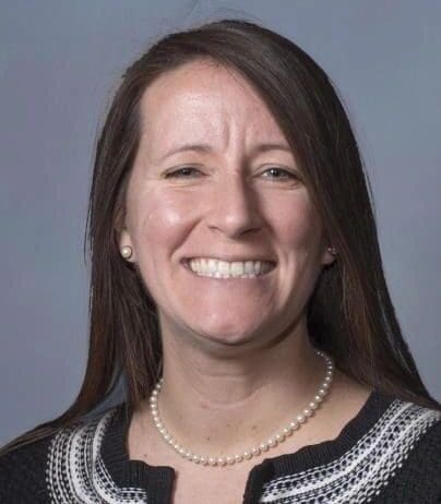 A woman with long hair and a necklace smiles.
