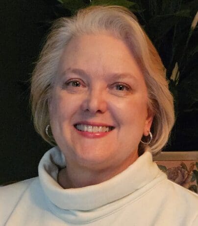 A woman with blonde hair wearing white is smiling.