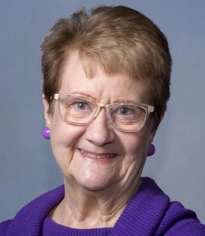 A woman with glasses and short hair wearing purple.