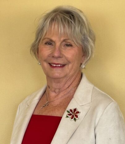 Smiling elderly woman with short blonde hair in a white blazer and red top.