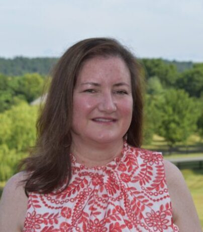 Woman smiling outdoors with trees in the background.