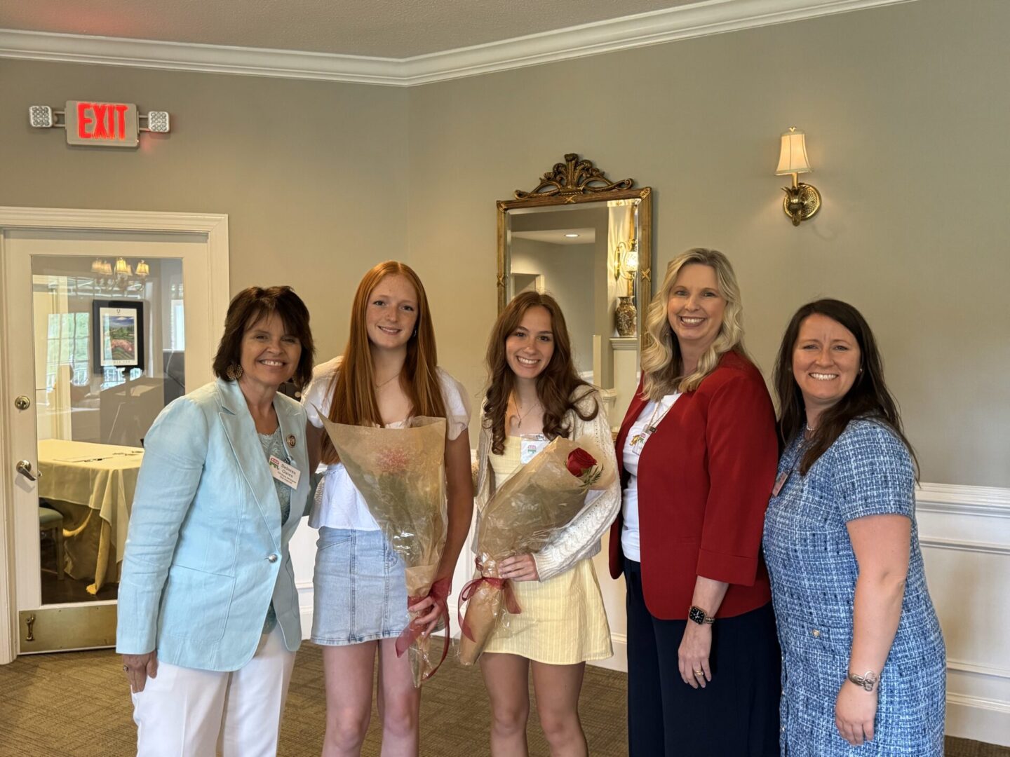 A group of five women posing indoors, smiling.